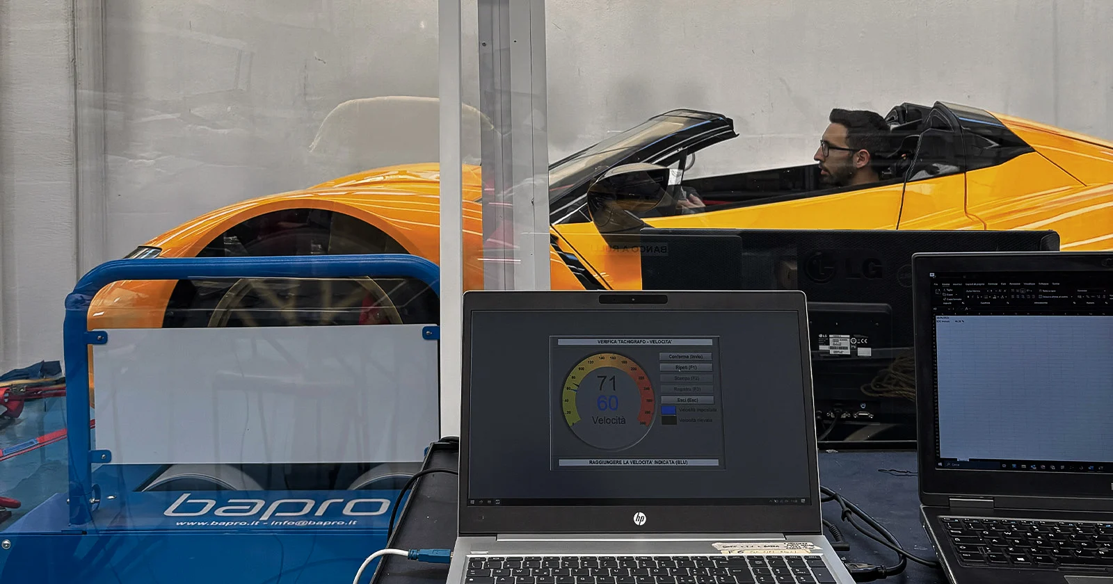 Sports car undergoing homologation testing with a man in the driver seat and two monitors displaying real time technical data